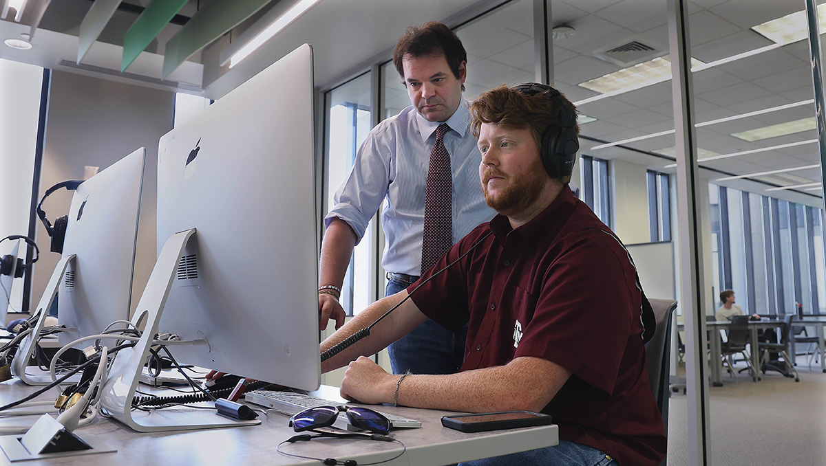 Two people, including Dr. Rossi, working together at a computer in the Studio's computer lab space, editing